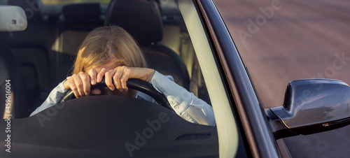 Exhausted female driver with blond hair leaning head on steering wheel while sitting in side modern car. Mature woman feeling tired after lomg distance driving. photo