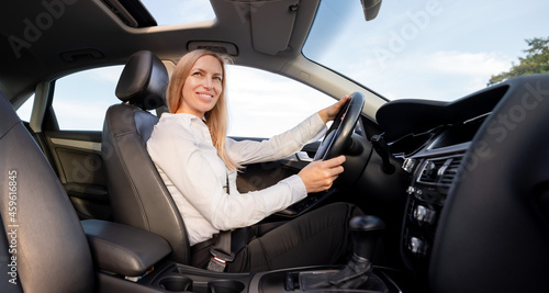Attractive mature woman in formal clothes fastening with seatbelt while driving modern car. Caucasian business lady with blond hair enjoying her way to work. © MYDAYcontent