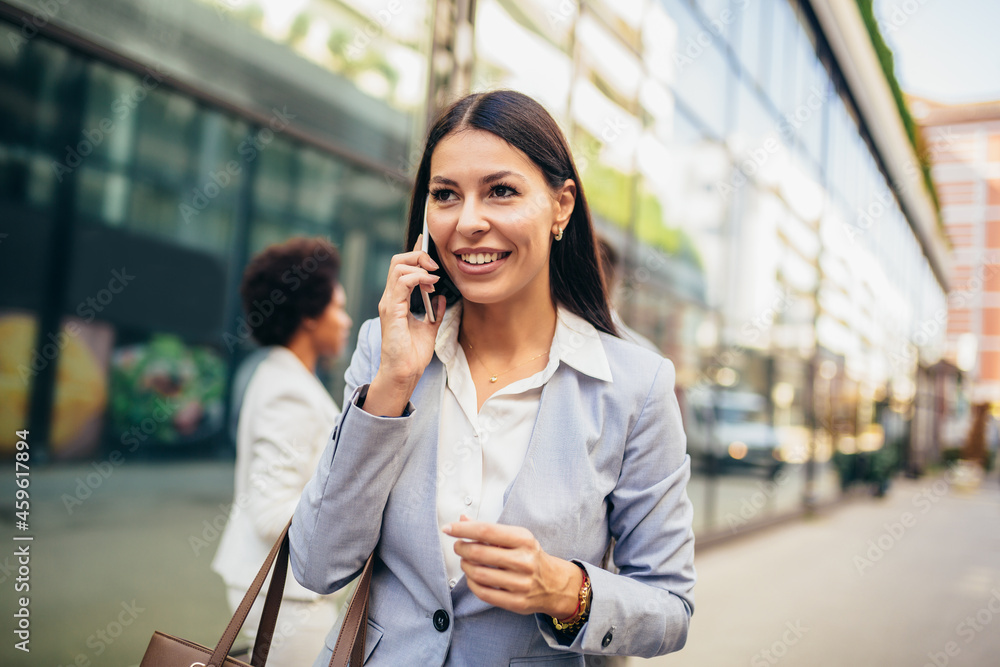 Portrait of beautiful smiling female in fashion office clothes talking on phone while standing outdoors. Portrait of beautiful smiling female in fashion office clothes talking on phone while standing outdoors.