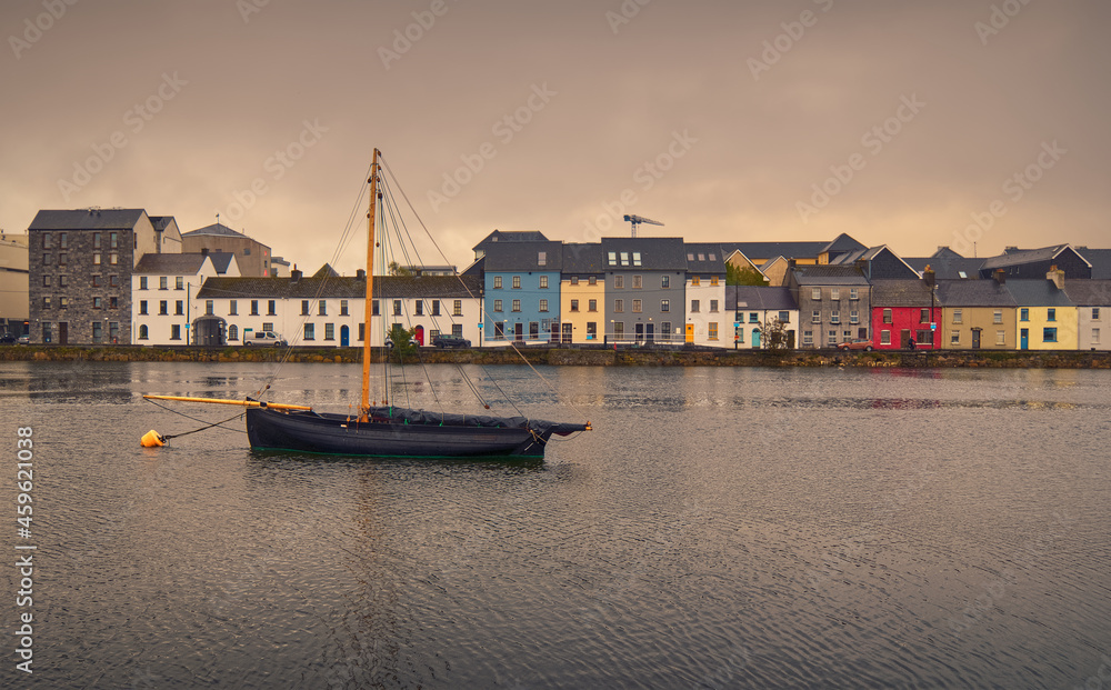 Beautiful cityscape scenery with old wooden fishing boat named Galway hooker in the Corrib River with colorful houses in the background at Claddagh in Galway city, Ireland 