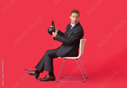 Young businessman with steering wheel sitting on chair against color background