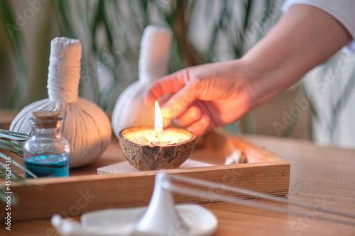 candle with the scent of coconut on a wooden table. Beautiful tropical spa concept. Cotton pouches with herbs for massage on wood background with green leafs. Herbal compress balls