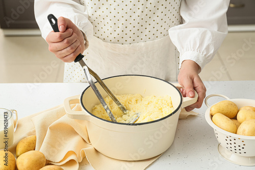 Woman preparing tasty mashed potatoes on table in kitchen, closeup photo