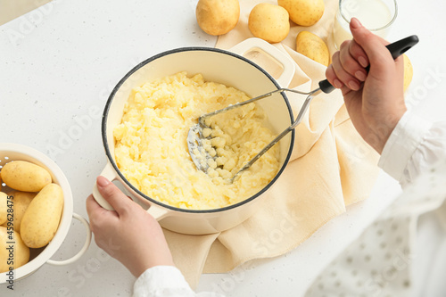 Woman preparing tasty mashed potatoes on light background, closeup photo