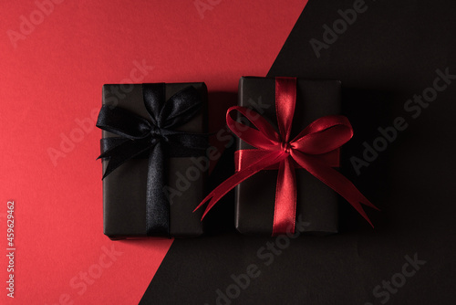 Black Friday sale shopping concept, Top view of gift box wrapped in black paper and black bow ribbon, studio shot isolated on red and dark background