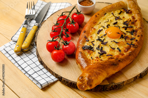 Board with tasty Ajarian khachapuri and tomatoes on wooden background photo