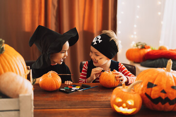 Boy and girl in suits paint faces on pumpkins