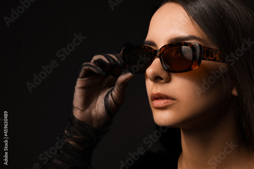 Young woman wearing stylish sunglasses on dark background