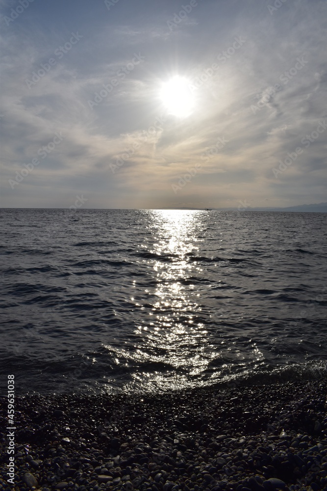 銀色の太陽と海面に光る波と丸い石の海岸