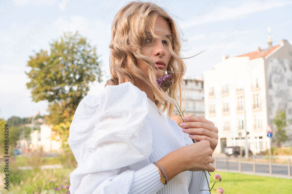 Fototapeta premium A portrait of a beautiful blond girl holding a purple flower close to her face.