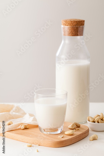 A glass and bottle of milk with nuts on white table.