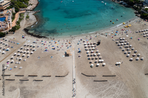 Aerial photo of the Spanish island of Ibiza showing the beautiful beach front with people on and the beach at Cala Llonga in the summer time in the Balearic Islands, Spain