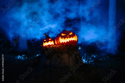 Pumpkin lanterns with Jack's carved faces on the traditional horror festival in the forest with smoke.