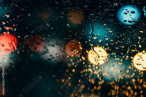 Rain Humidity night traffic lights of big city, rain drops on car windshield glass, focus on raindrops. Rain background of a night blurred city. Rainy night weather
