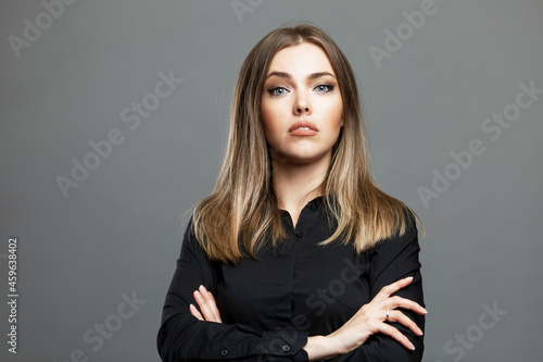 Arrogant beautiful woman with crossed arms. Spectacular blonde in a black shirt. Gray background.