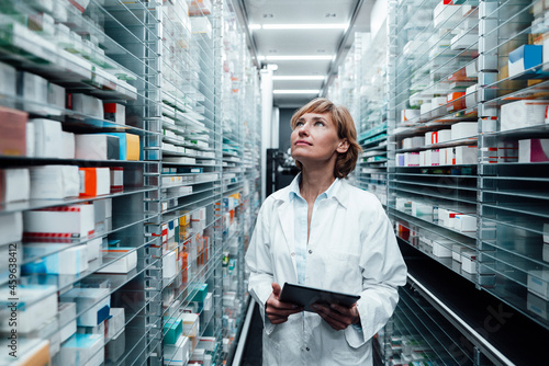 Female pharmacist looking at medicine while holding digital tablet at pharmacy store photo