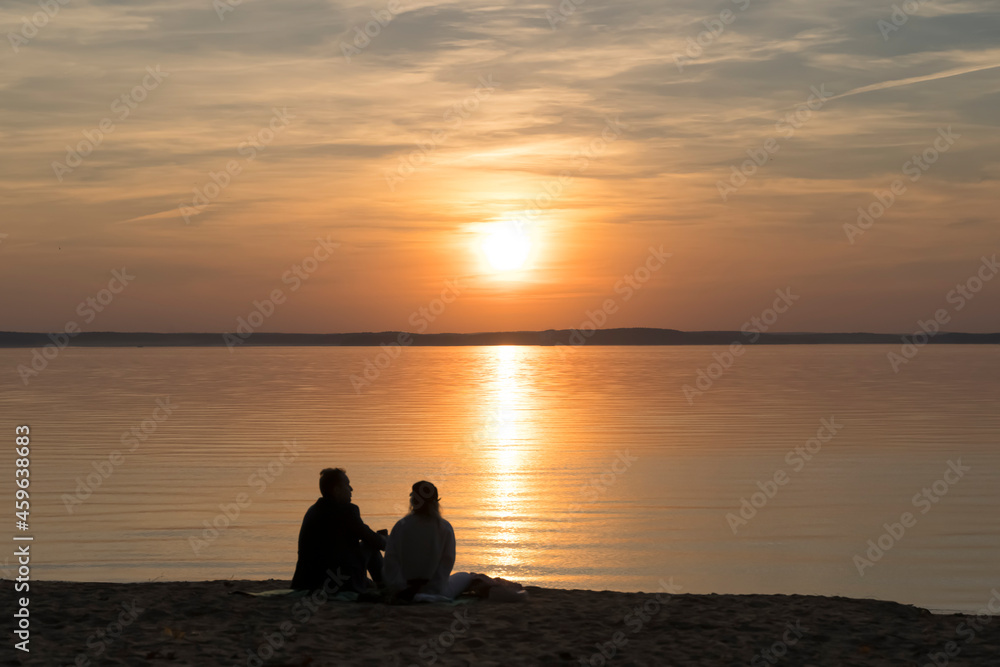 Couple on the shore of the lake during summer sunset and beautiful evening sky. Romance, love, relationships, friendship. Couple on the shore of the lake during summer sunset and beautiful evening sky. Romance, love, relationships, friendship.