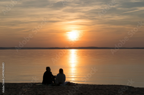 Couple on the shore of the lake during summer sunset and beautiful evening sky. Romance, love, relationships, friendship.
