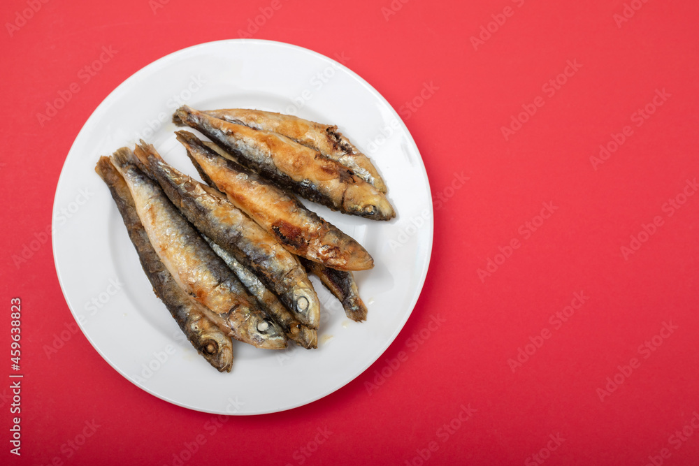 fried small sardines on white plate on red fried small sardines on white plate on red