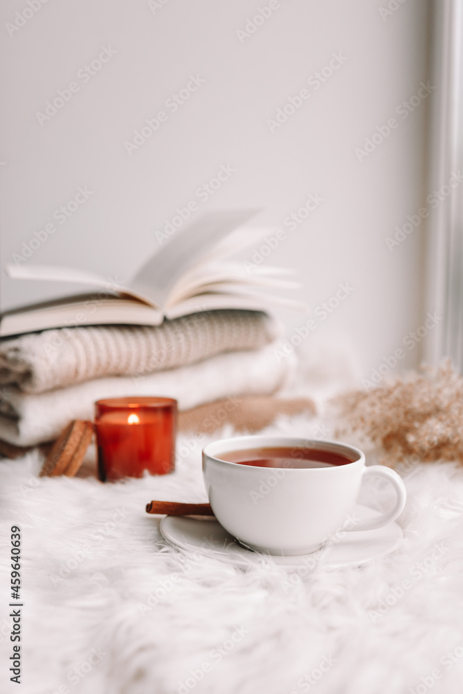 A cup of tea on the window with burning candles and sweaters.