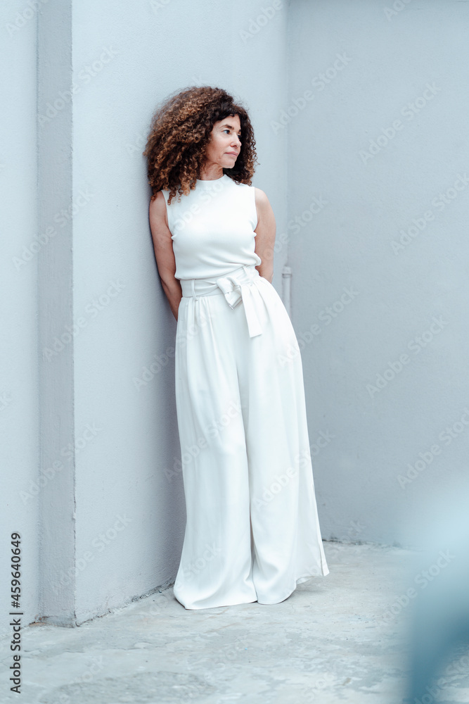 Mature businesswoman with curly hair standing by gray wall Mature businesswoman with curly hair standing by gray wall