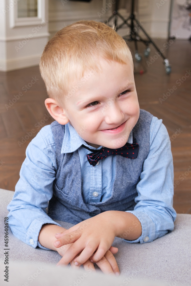 Vertical portrait of a five-year-old blonde boy in a shirt, vest and bow tie. Close-up of the child's face. The boy smiles and squints. Vertical portrait of a five-year-old blonde boy in a shirt, vest and bow tie. Close-up of the child's face. The boy smiles and squints.