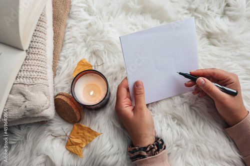 The girl writes a letter on the background of a candle. Home comfort.