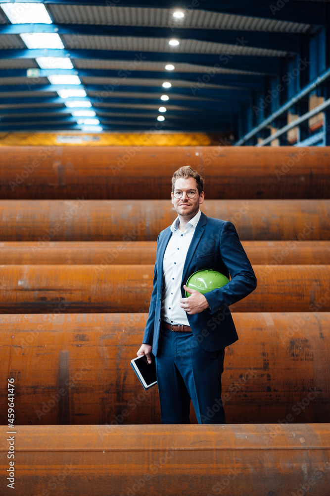 Male professional with digital tablet and hardhat standing at steel pipes Male professional with digital tablet and hardhat standing at steel pipes