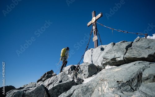 A woman in hiking outfit reaching the cross on Grossglockner, highest mountain in Austria. Clear day. Achievement. Girl on the top of peak