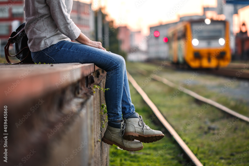 Obraz premium Traveler waiting for train at railway station. Woman with hiking boots sitting at railroad station. Solo travel concept