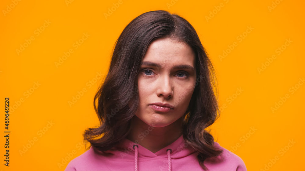 Fototapeta premium offended woman in pink hoodie looking at camera isolated on yellow