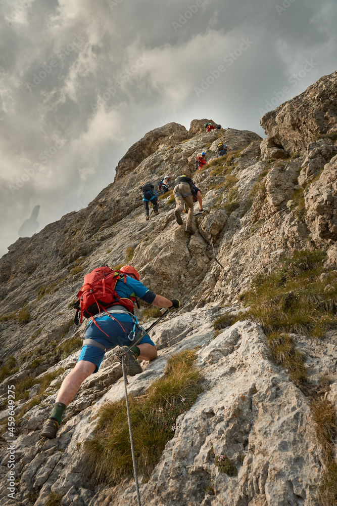 mixed gender group of climbers heading up a steep rock face the via ferrata Rodella near Sella Pass in South Tyrol, Dolomites, Italy