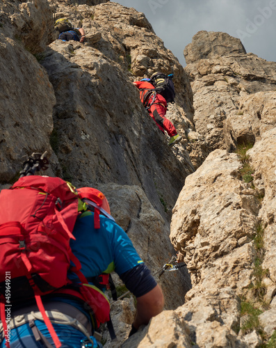 mixed gender group  of climbers in a via ferrata named rodella in the dolomites of south tyrol, italy, with colorful attire, rucksacks and helmets