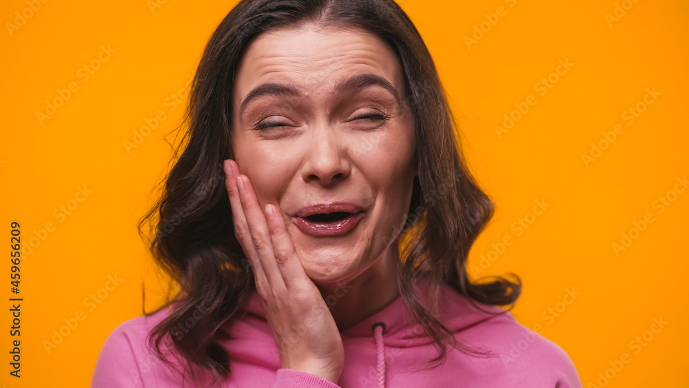 amazed and excited woman touching face while laughing isolated on yellow amazed and excited woman touching face while laughing isolated on yellow