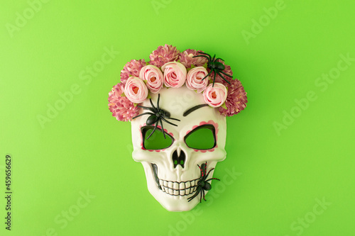 Sugar skull with colorful flowers and black spiders against green background. Minimal Halloween or Santa Muerte concept. Flat lay.