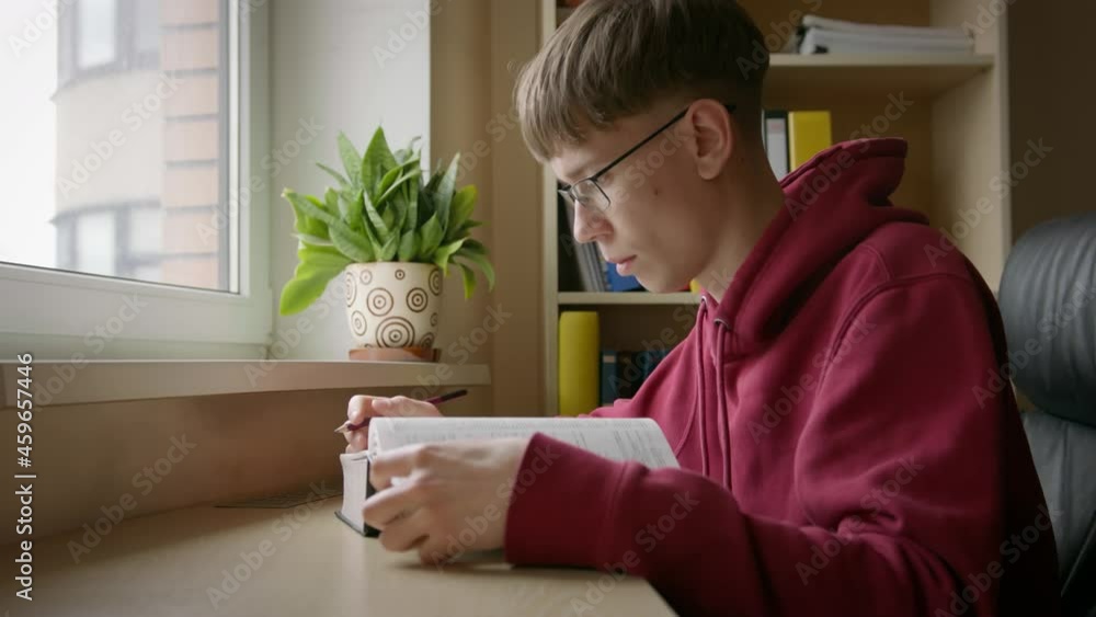 Young guy, wearing eyeglasses, reading book, making notes by pencil Young guy, wearing eyeglasses, reading book, making notes by pencil