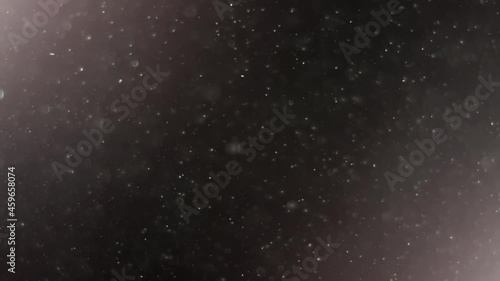 A suspension of white particles in the air with color lighting on a black background. Some of the particles are blurred in a beautiful bokeh. 4K background for your videos in various mixing modes.