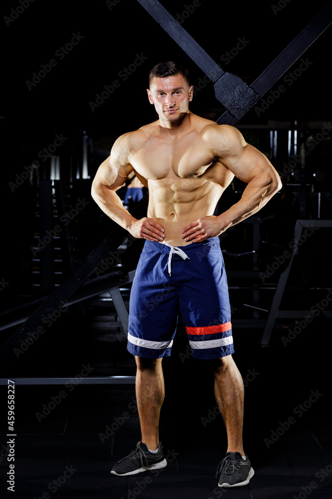 Fototapeta premium Young bodybuilder with great muscles posing in gym