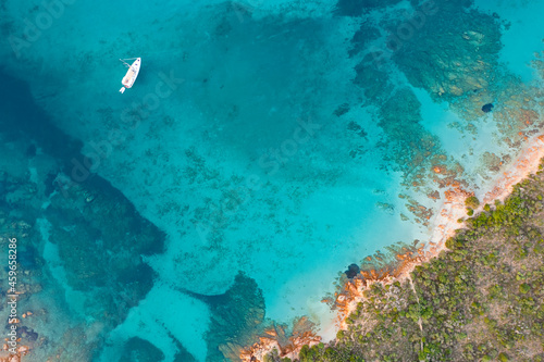 View from above, stunning aerial view of a green and rocky coastline with a sailboat sailing on a turquoise, crystal clear water. Liscia Ruja, Costa Smeralda, Sardinia, Italy..