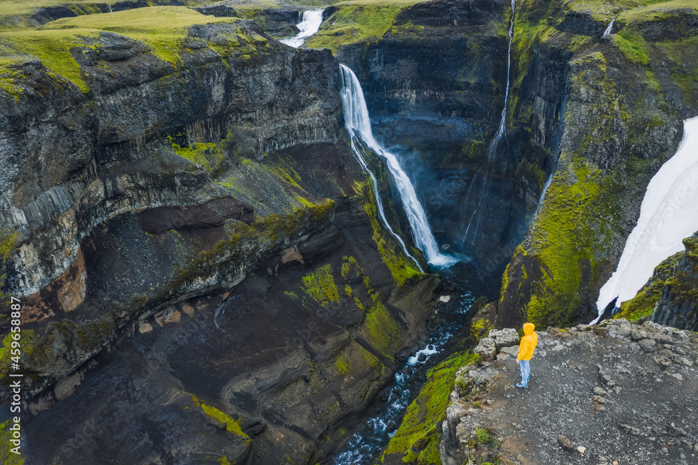 Man in yellow coat enjoying Haifoss Waterfall in Landmannalaugar canyon, Iceland. Aerial panoramic drone view