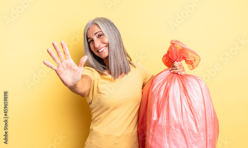 middle age pretty woman smiling and looking friendly, showing number five. plastic garbaje bag photo