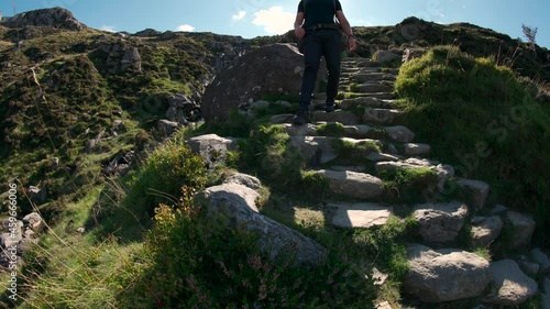 A man with backpack walkign down stone mountain steps in bright sunshine photo