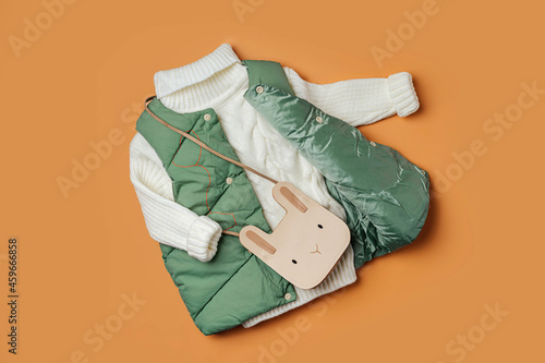 Green  waistcoat  with warm sweater on orange background. Stylish childrens outerwear. Winter fashion outfit