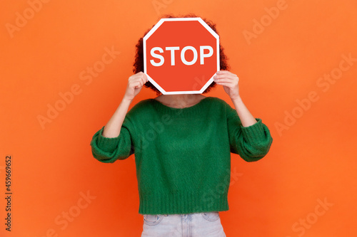 Quadro su tela Unknown woman with wearing green casual style sweater hiding her face behind red stop traffic symbol, warning, avoids forbidden actions