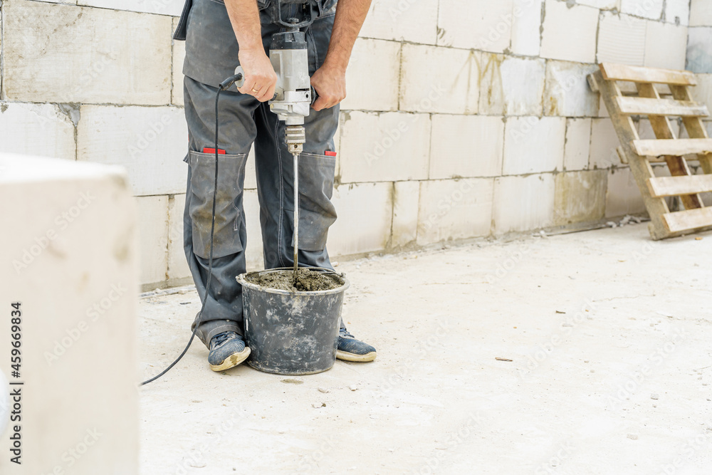 young male bricklayer builder kneads concrete, for laying aerated concrete blocks, using a construction mixer on a construction site. Free space for text. Copy space