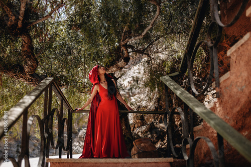 Woman in little red riding hood costume looking up while standing in front of trees