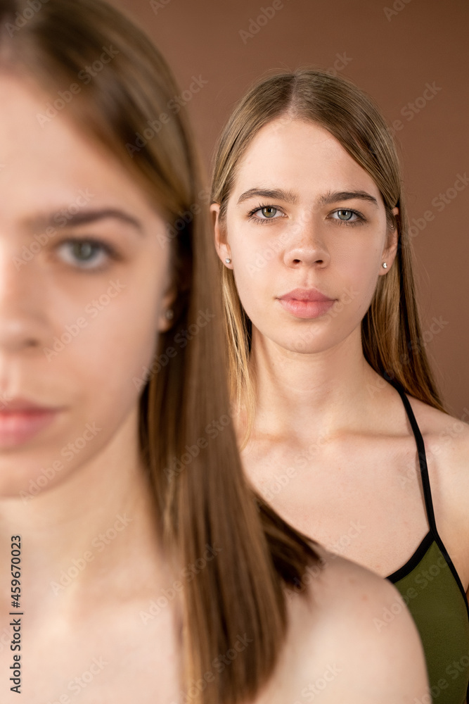 One of blond pretty twin girls standing behind her sister in front of camera One of blond pretty twin girls standing behind her sister in front of camera