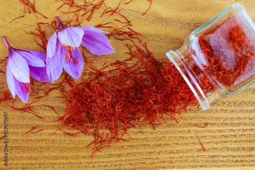 Saffron stigmas scattered on a wooden surface from a glass bottle. Saffron crocus flowers. photo