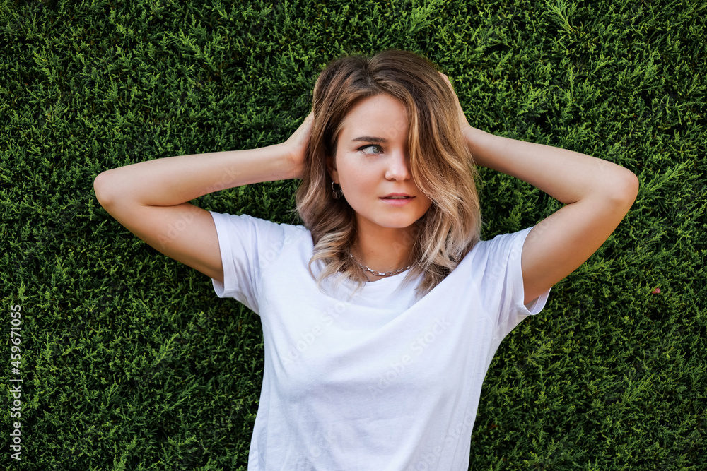 Young woman in white shirt with natural makeup standing by green hedge Young woman in white shirt with natural makeup standing by green hedge