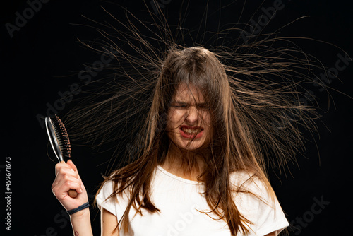 Woman with static long hair up in the air and a hair brush, on black background.
